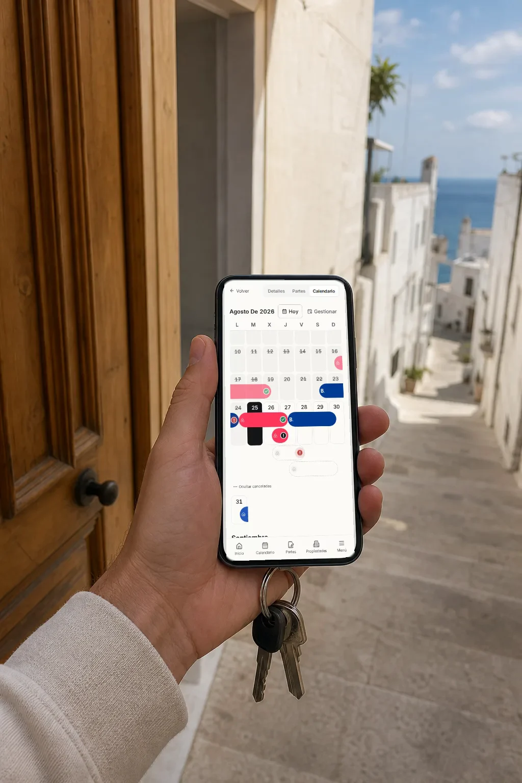 Una mano sostiene un móvil frente a la puerta de un apartamento mediterráneo; en la pantalla, el calendario de reservas de Regi con las estancias de agosto.